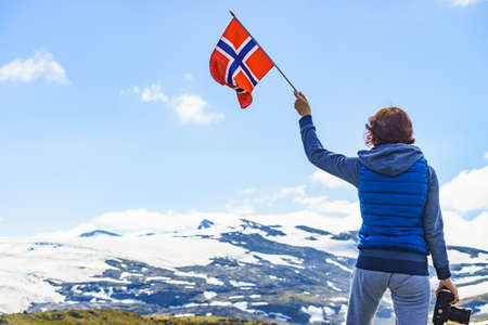Tourist woman enjoy mountains landscape, holding Norwegian flag and photo camera. National tourist scenic route 55 Sognefjellet, Norwayの写真素材