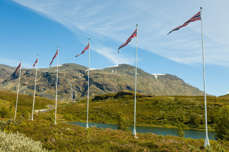 Norwegian flags waving against mountains landscape. National tourist scenic route 55 Sognefjellet...