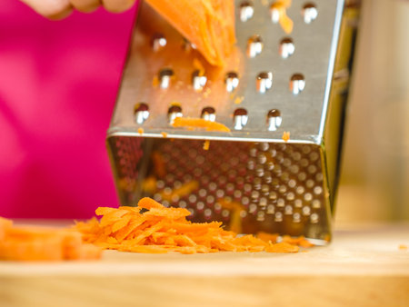 Unrecognizable woman grating carrot on metal grater, kitchen utensil making food preparing healthy vegetable salad.の写真素材