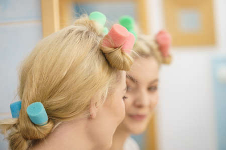 Blonde woman using hair rollers to create beautiful hairstyle on her hairdo.の写真素材