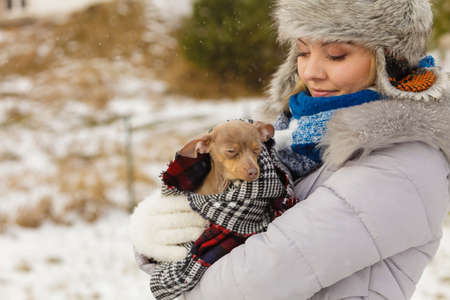 Young woman wrapped her best friend little dog in warm blanket scarf to warm him in cold snowy winter day. Animal protection save. Adoption conceptの写真素材