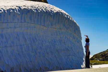 Tourist woman with camera looking at high snow wall on mountain road Aurlandsfjellet in Norway, summer timeの写真素材