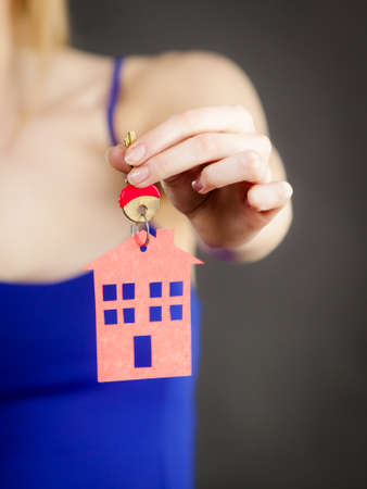 Young woman holding new house key with red home shape. Real estate and housing concept.の写真素材