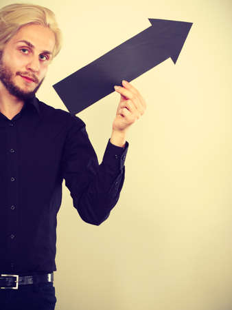 Planning, directions, choices concept. Man holding black arrow pointing right up. Indoor shot on light backgroundの写真素材