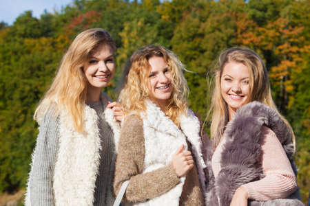 Three fashionable women wearing sweaters during warm autumnal weather spending their free time in park. Fashion models outdoorの写真素材