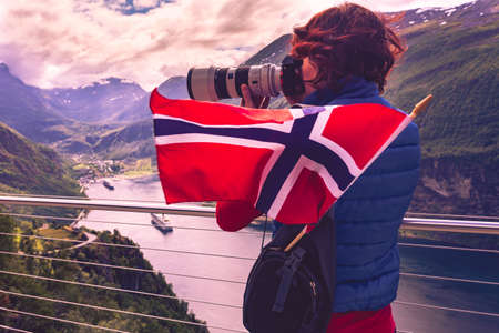 Tourism holidays picture and traveling. Woman tourist enjoying fjord landscape Geirangerfjord from Ornesvingen eagle road viewpoint, taking photo with camera, Norway.の写真素材