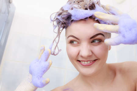 Funny crazy woman having coloring shampoo on her hair, purple washing product. Toning blonde color at home concept.の写真素材