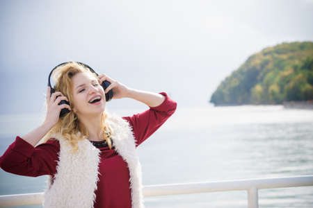 Happy joyful woman listening to music while being outdoor. Teenage female wearing headphones having fun on a walk.の写真素材