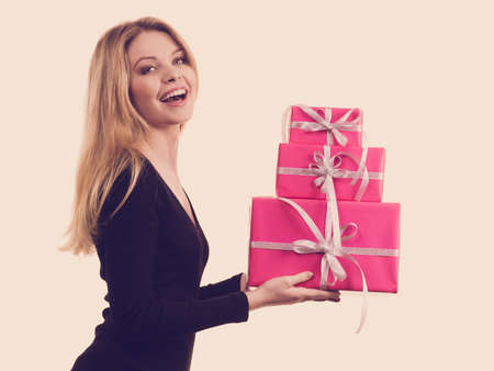People celebrating xmas love and happiness concept. Cheerful blonde girl holding presents pile of pink gift boxes, side viewの写真素材