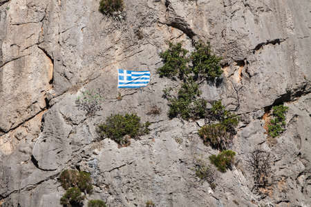 The white blue national flag of Greece hanging on stone wall mountain hills.の写真素材