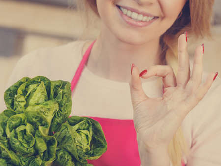Happy young woman, cooking chef showing holding green lettuce. Female loving vegetables about to cook.の写真素材