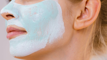 Young woman with white green mud mask on her face. Teen girl taking care of oily skin, cleaning the...