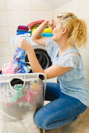 Unhappy woman in bathroom with big basket of dirty stink clothing, disgusting laundry, closed her nose by hand. Hard work, dirty job, household duty.の写真素材