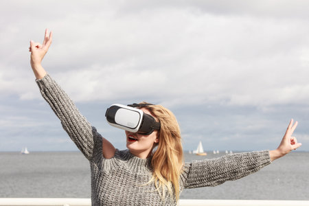 Young woman testing VR glasses outside. Female wearing virtual reality headset during spring...