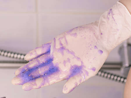Person coloring hair at home, having purple washing shampoo product on white latex protective glove under the shower.の写真素材