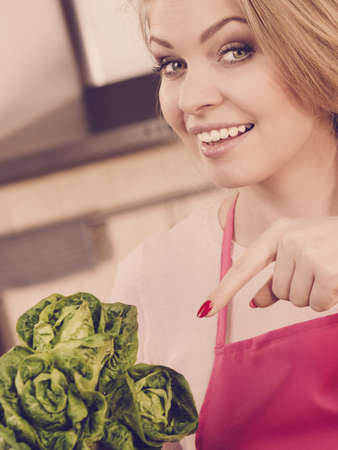 Happy young woman, cooking chef showing holding green lettuce. Female loving vegetables about to cook.の写真素材