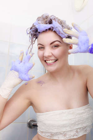 Funny crazy woman having coloring shampoo on her hair, purple washing product. Toning blonde color at home concept.の写真素材