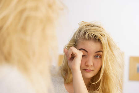 Young blonde female feeling dull and tired after waking up. Woman yawning being sleepy in bathroom.の写真素材