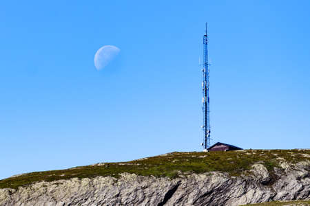 Telecommunications tower mast wireless technology in mountains and moon on skyの写真素材