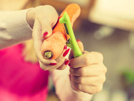 Woman peeling vegetables using food peeler. Cooking female preparing carrot before serving.の写真素材