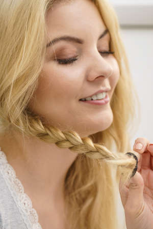 Young pretty blonde woman creating her hairstyle, making braid. Lovely female getting readyの写真素材