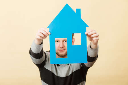 Thought about house new flat. Young handsome positive man with paper model of real estate. Smiling guy dreaming thinking about his own place to live.の写真素材