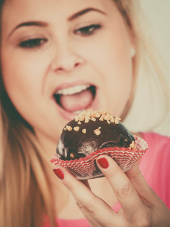Diet, sweets, food concept. Woman holding delicious chocolate cupcake with peanut frosting, having...