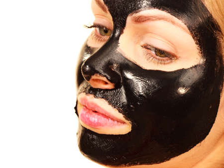 Young woman with carbo detox black peel-off mask on her face, on white. Teen girl taking care of oily skin, cleaning the pores. Beauty treatment. Skincare.の写真素材