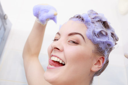 Funny crazy woman having coloring shampoo on her hair, purple washing product. Toning blonde color...