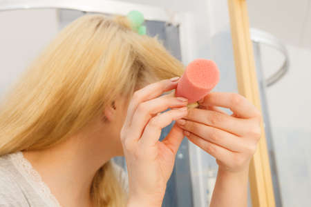 Blonde woman using hair rollers to create beautiful hairstyle on her hairdo.の写真素材