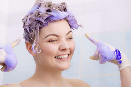 Woman wearing latex protective gloves while applying purple toner shampoo on her blonde hair. Haircare coloring at home concept.