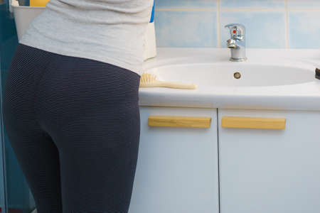 Unrecognizable woman wearing dark leggings standing in front of bathroom sink about to clean.の写真素材