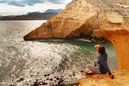 Tourist adult woman relaxing on yellow sand formations of Cocedores Beach. Mediterranean sea, Murcia region Spain.の写真素材