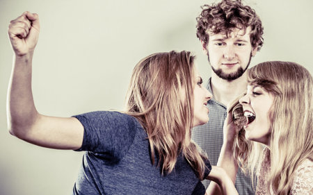 Aggressive mad women fighting over man. Young jealous girls wooing guy. Violence.