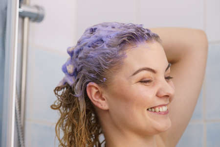 Woman having purple shampoo foam on her head under the shower. Female toning blonde hair using colored shampoo.の写真素材