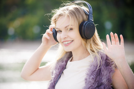 Happy joyful woman listening to music while being outdoor. Teenage female wearing headphones having fun on a walk.の写真素材