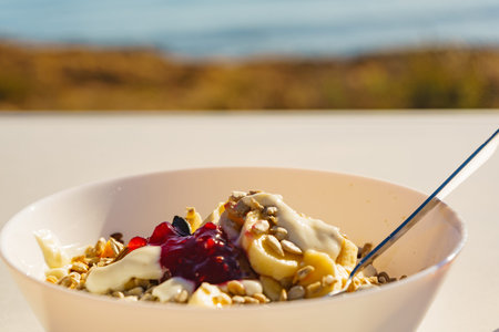 Healthy breakfast on nature. Oatmeal granola with yogurt, banana fruits in bowl, sunny morning,...