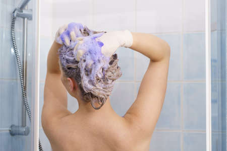 Woman applying coloring shampoo on her hair. Female having purple washing product. Toning blonde color at home.の写真素材