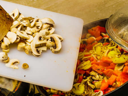Making delicious dinner food meal. Adding fresh sliced mushrooms to hot pan with mixed vegetables.の写真素材