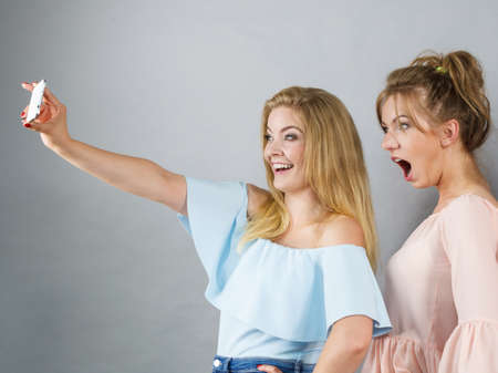 Fashionable two women taking selfie self picture using smartphone having fun enjoying friends time.の写真素材