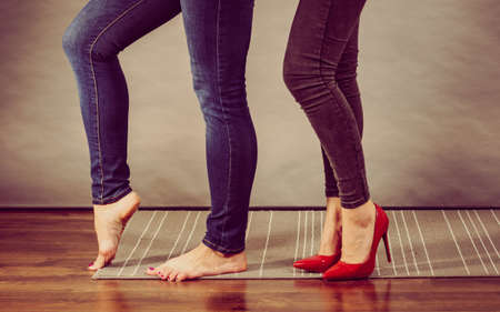 Two women legs, one woman barefoot and the other wearing red high heels shoes. Foot size problem.の写真素材