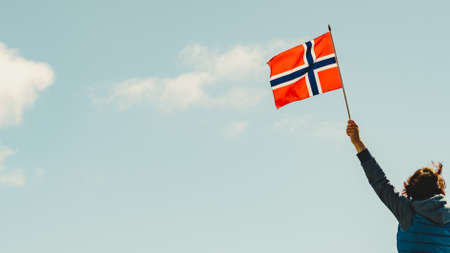 Tourist woman holding norwegian flag against blue skyの写真素材