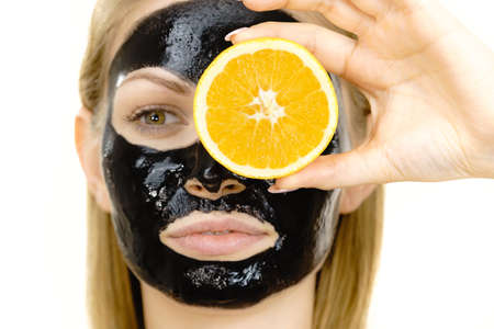 Woman with carbo detox black peel-off mask on face holding orange fruit. Teen girl taking care of oily skin, cleaning the pores. Beauty treatment. Skincare.の写真素材