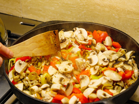 Making delicious dinner food meal. Adding fresh sliced mushrooms to hot cast iron frying pan with mixed vegetables.の写真素材