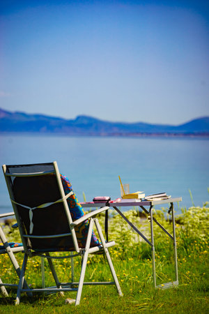 Camping portable chairs and table with books on on norwegian fjord shore. Holidays relaxation on...