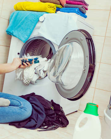 Woman in bathroom sorting different colored clothes laundry for washing in machine, using detergent pods gel capsules. Household duties chemicals objects.の写真素材