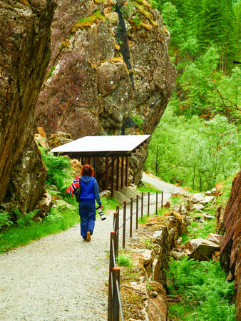 Tourist woman with norwegian flag and camera walking trough mountains path in Allmannajuvet area Sauda, Norway. Attraction along national tourist route Ryfylke.の写真素材