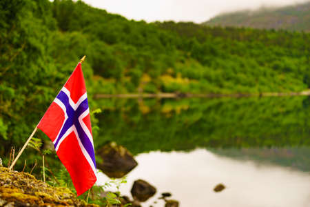 Norwegian flag waving outdoor on green nature. Green mounains hills with tarnの写真素材