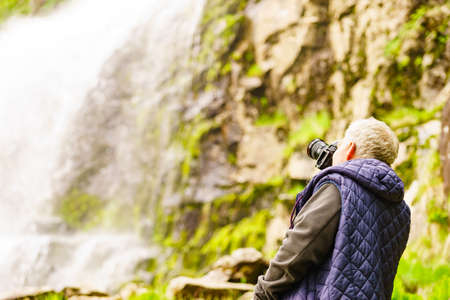 Tourist with camera taking travel picture at Svandalsfossen in Norway, powerful waterfall in norwegian mountains. National tourist Ryfylke route.の写真素材