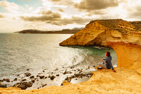 Tourist adult woman relaxing on yellow sand formations of Cocedores Beach. Mediterranean sea, Murcia...